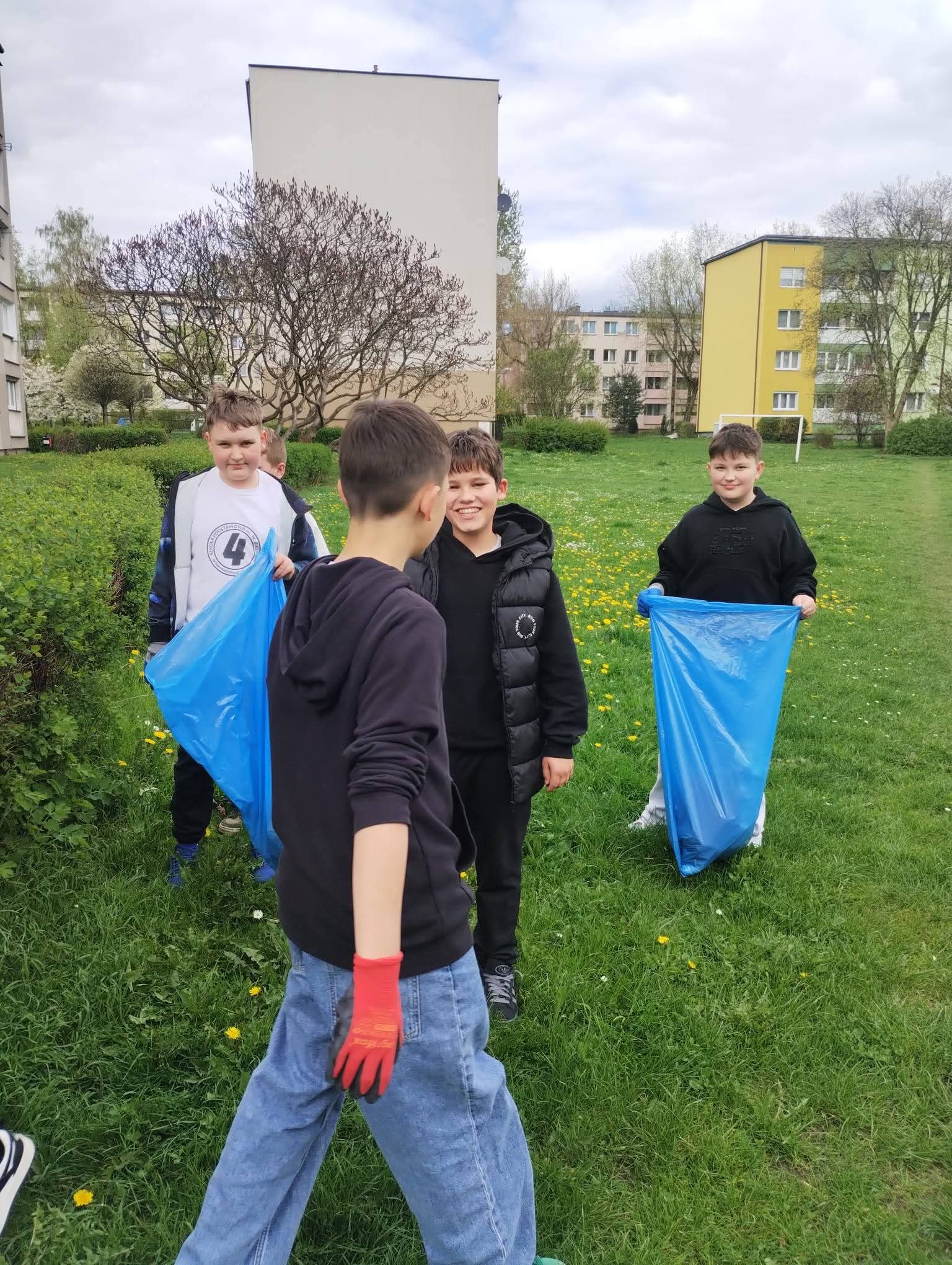 Chłopcy z niebieskimi workami zbierają śmieci na trawniku w parku.