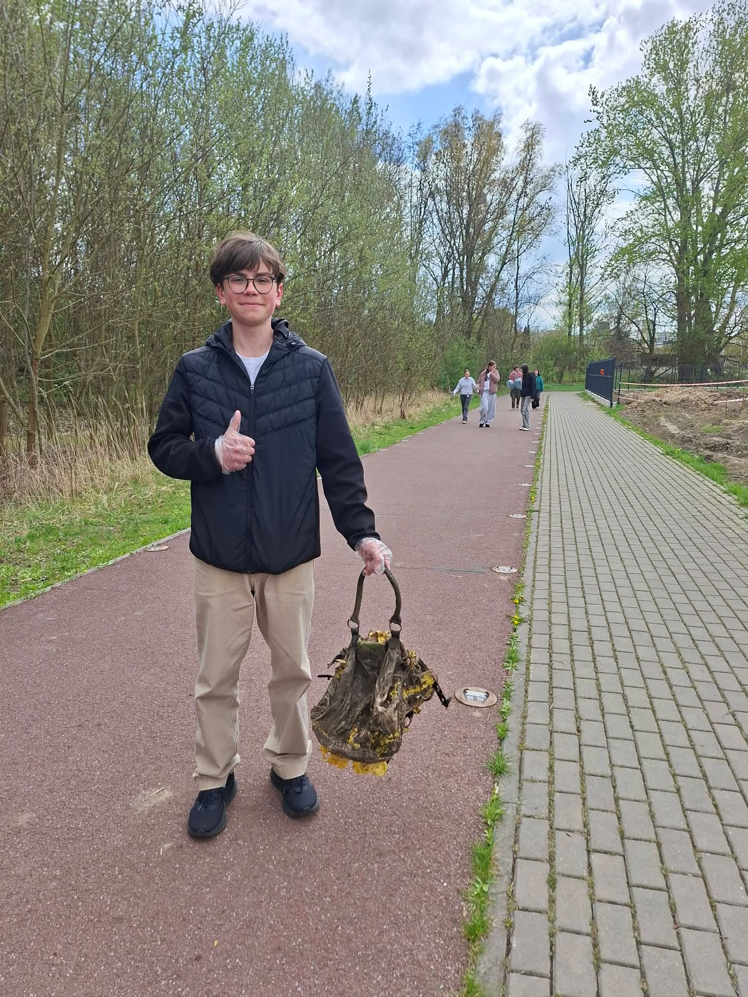 Chłopiec w rękawiczkach z workiem pełnym śmieci na ścieżce