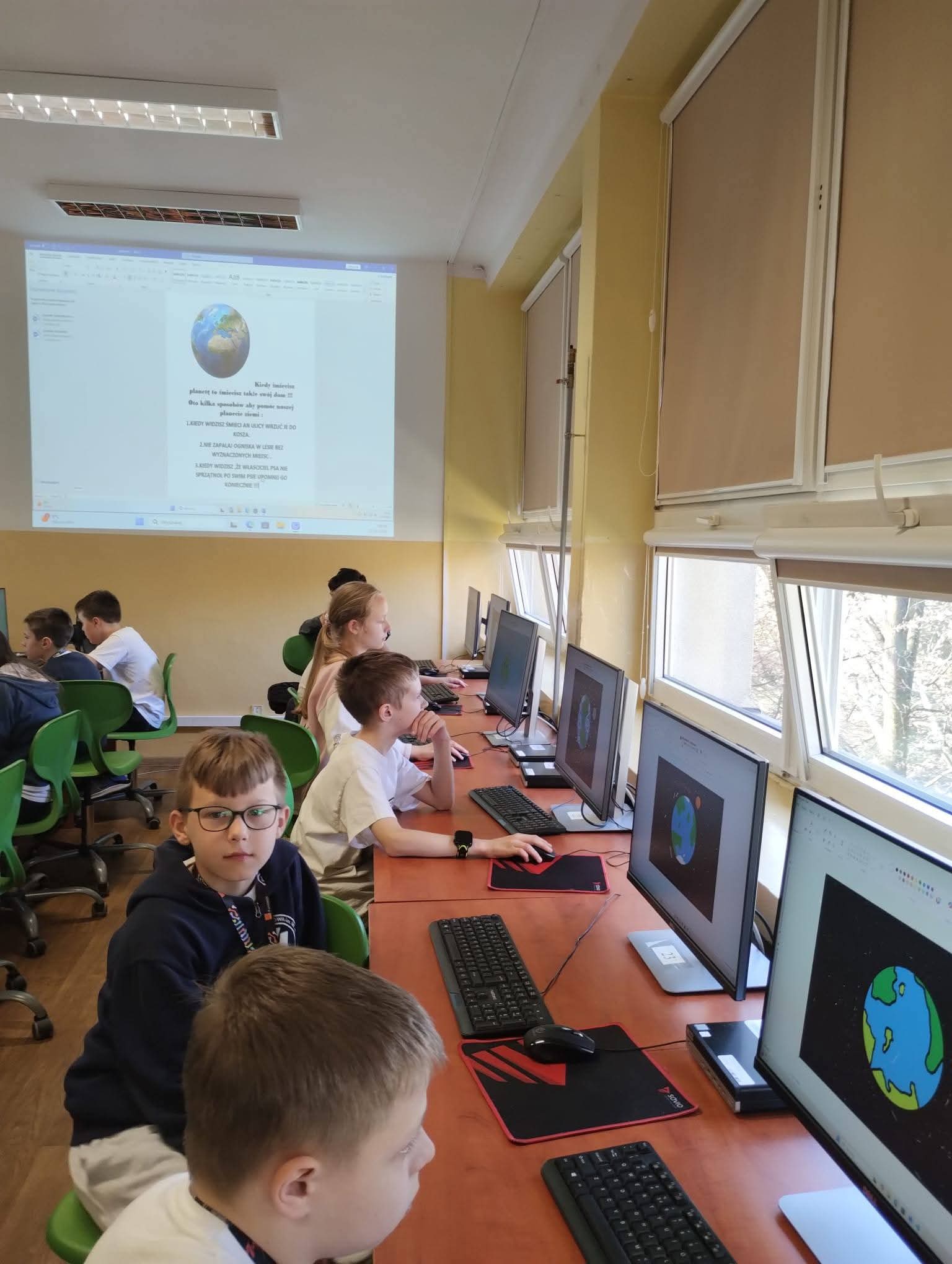 Dzieci uczą się o kosmosie na lekcji informatyki, patrząc na projektor z Ziemią.