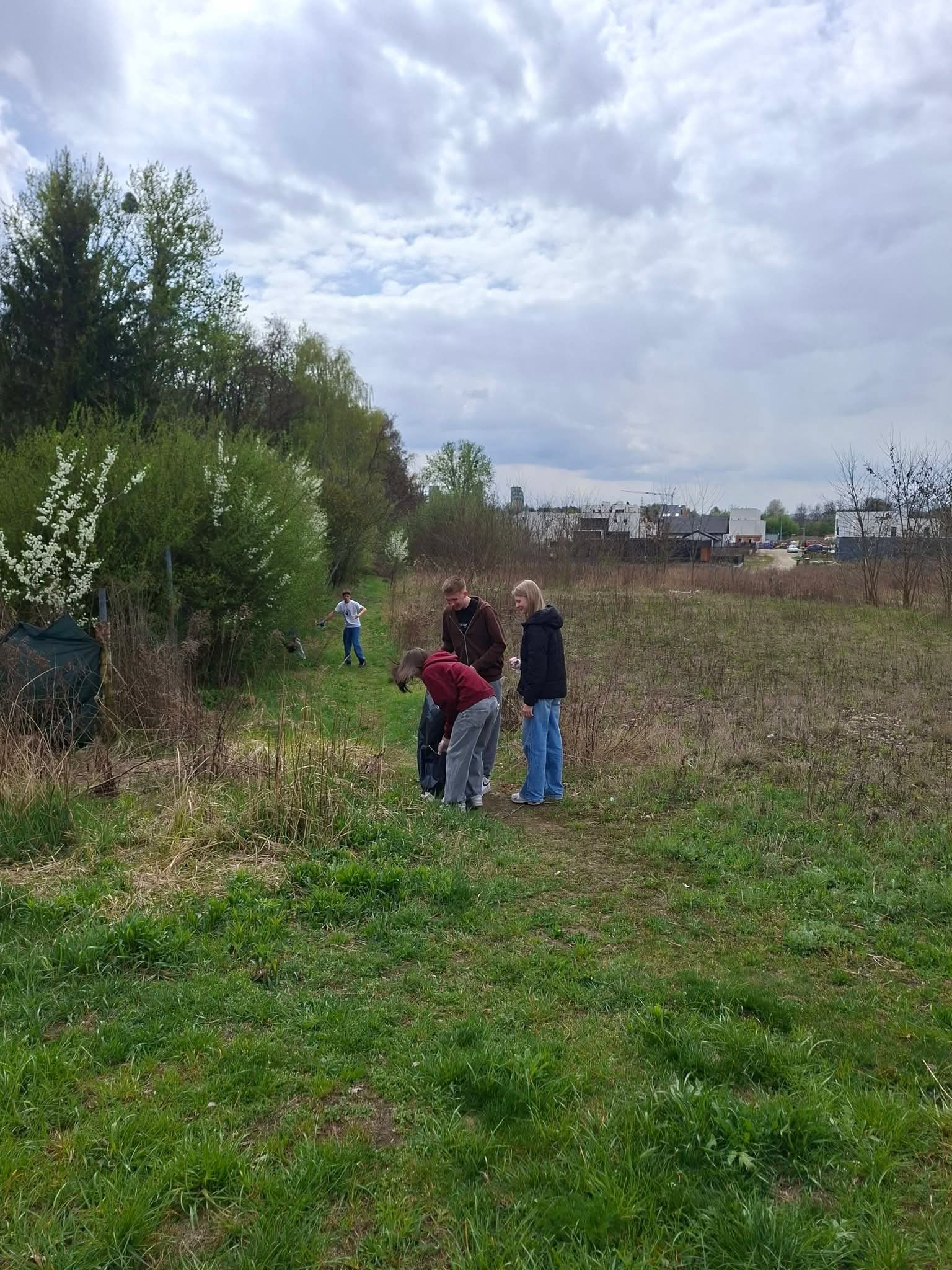 Grupa dzieci obserwuje coś na ziemi w trawiastym terenie z drzewami w tle.