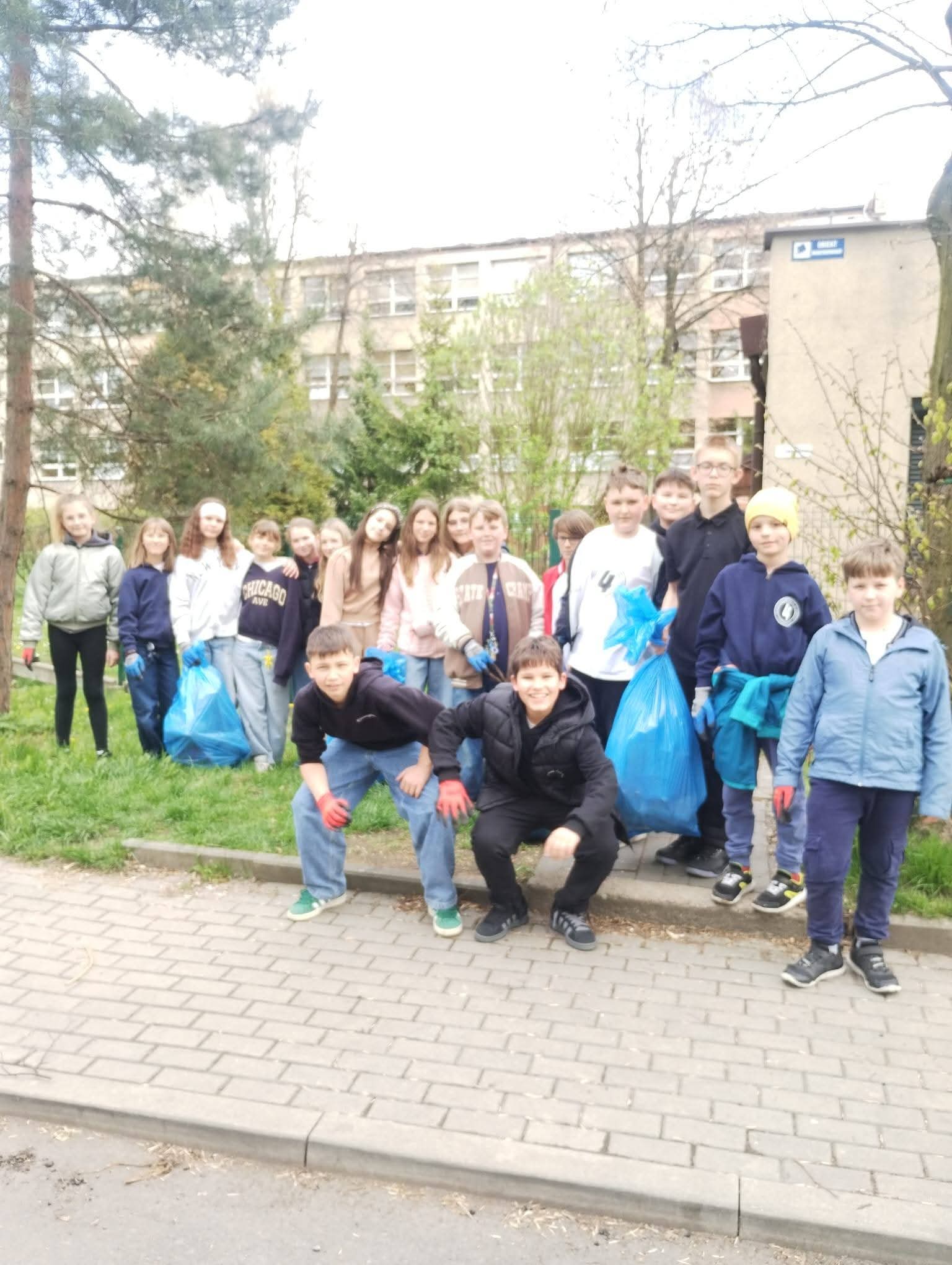 Grupa dzieci z workami na śmieci sprząta teren wokół szkoły