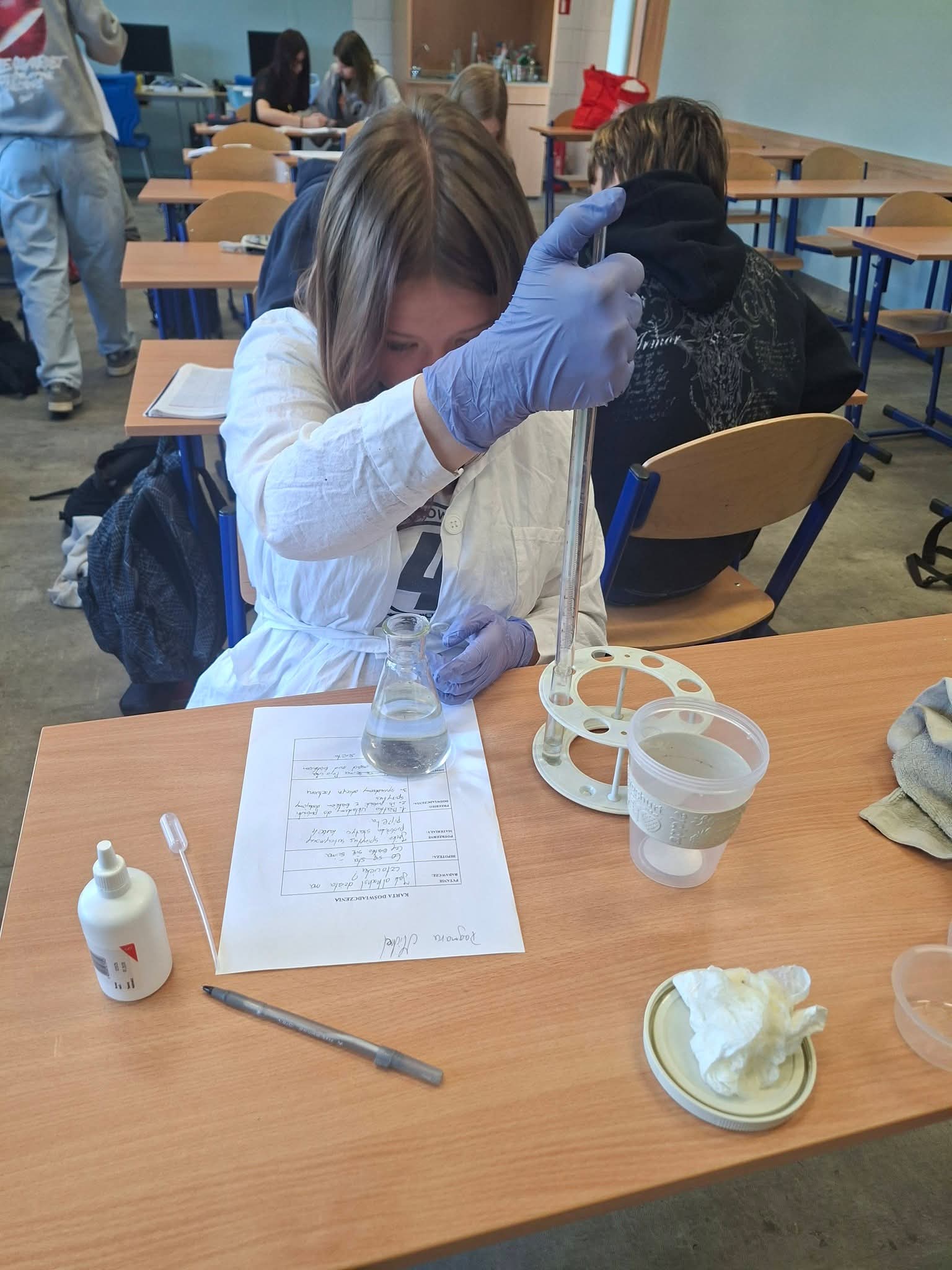 Dziewczynka w fartuchu laboratoryjnym wykonuje eksperyment z pipetą i kolbą
