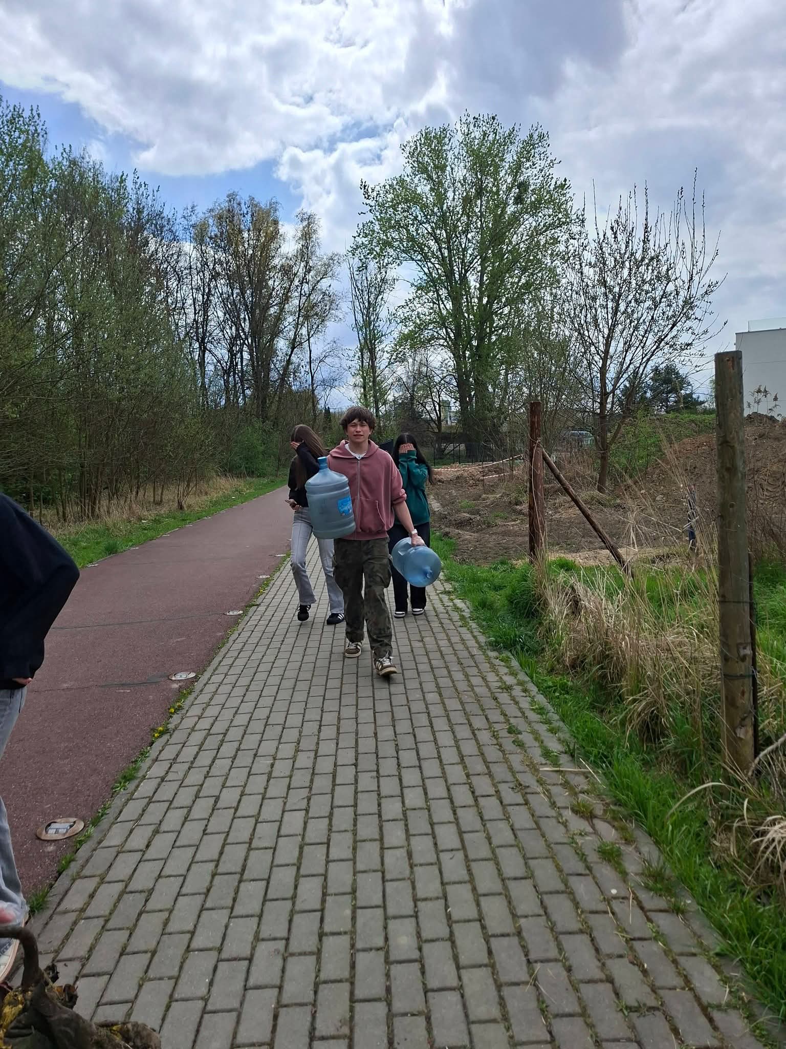 Młodzież niesie duże butle z wodą ścieżką w parku.