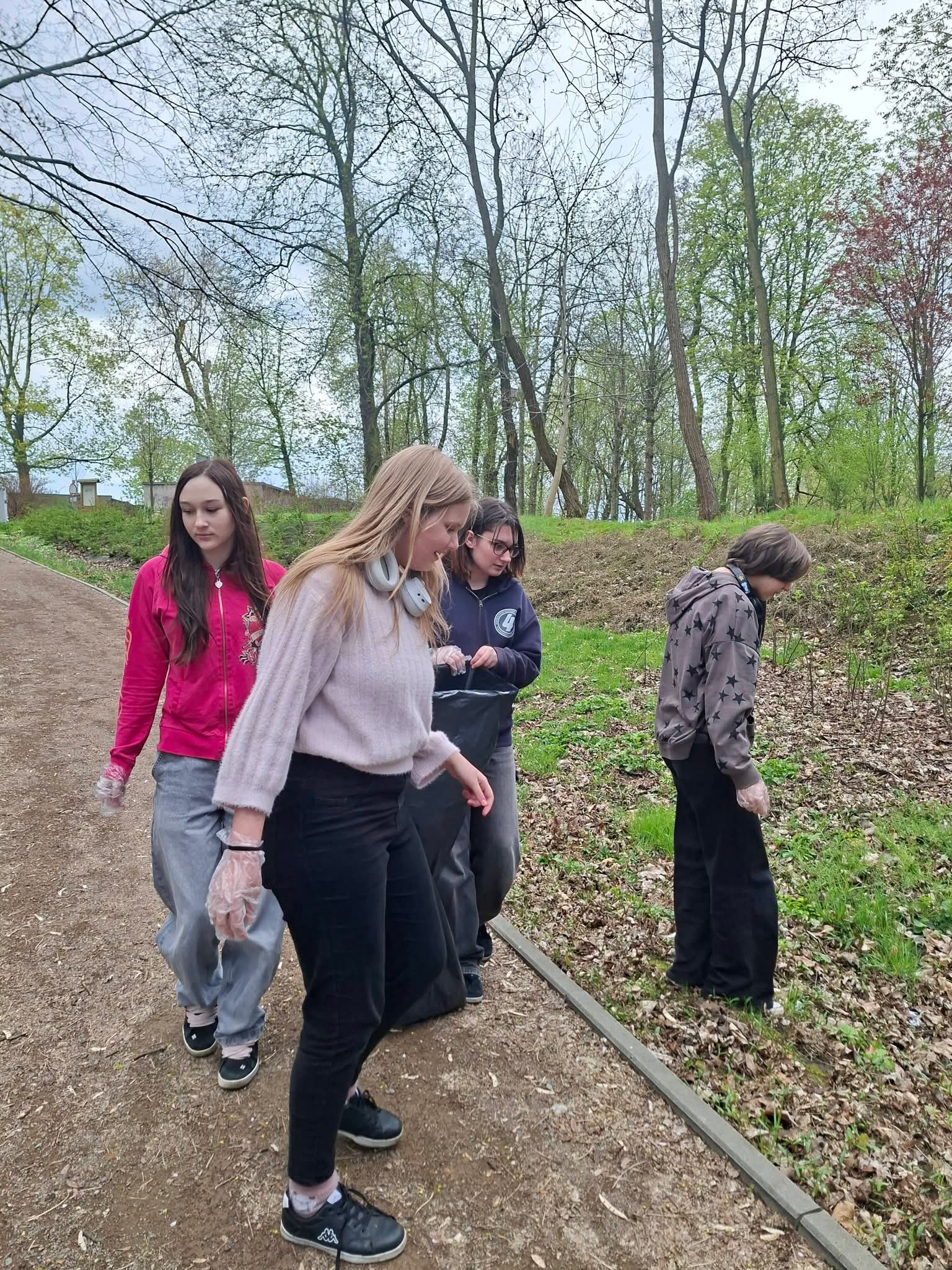 Młodzież zbiera śmieci w parku z workami na odpady.