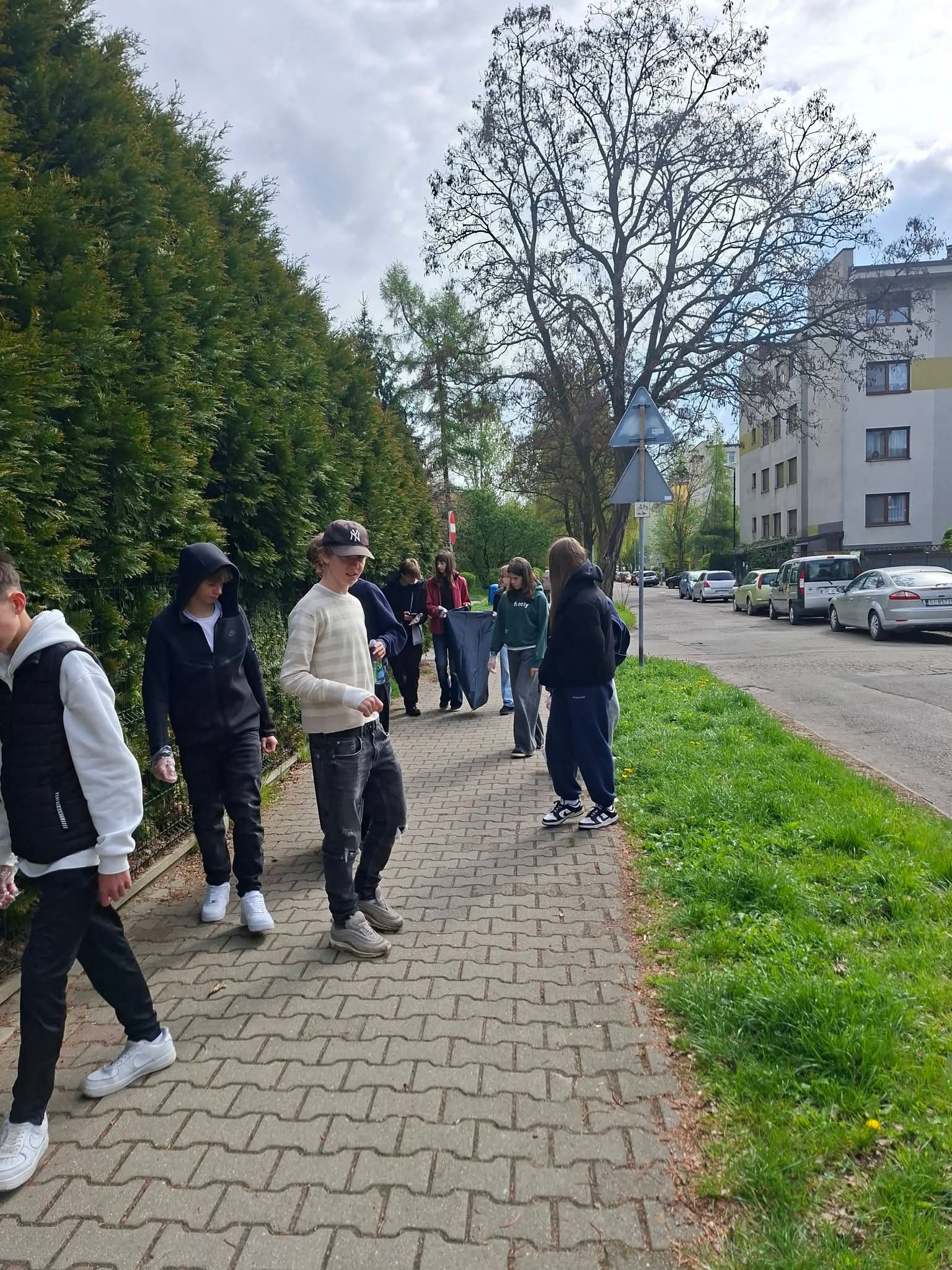 Grupa młodzieży zbiera śmieci na chodniku przy ulicy.