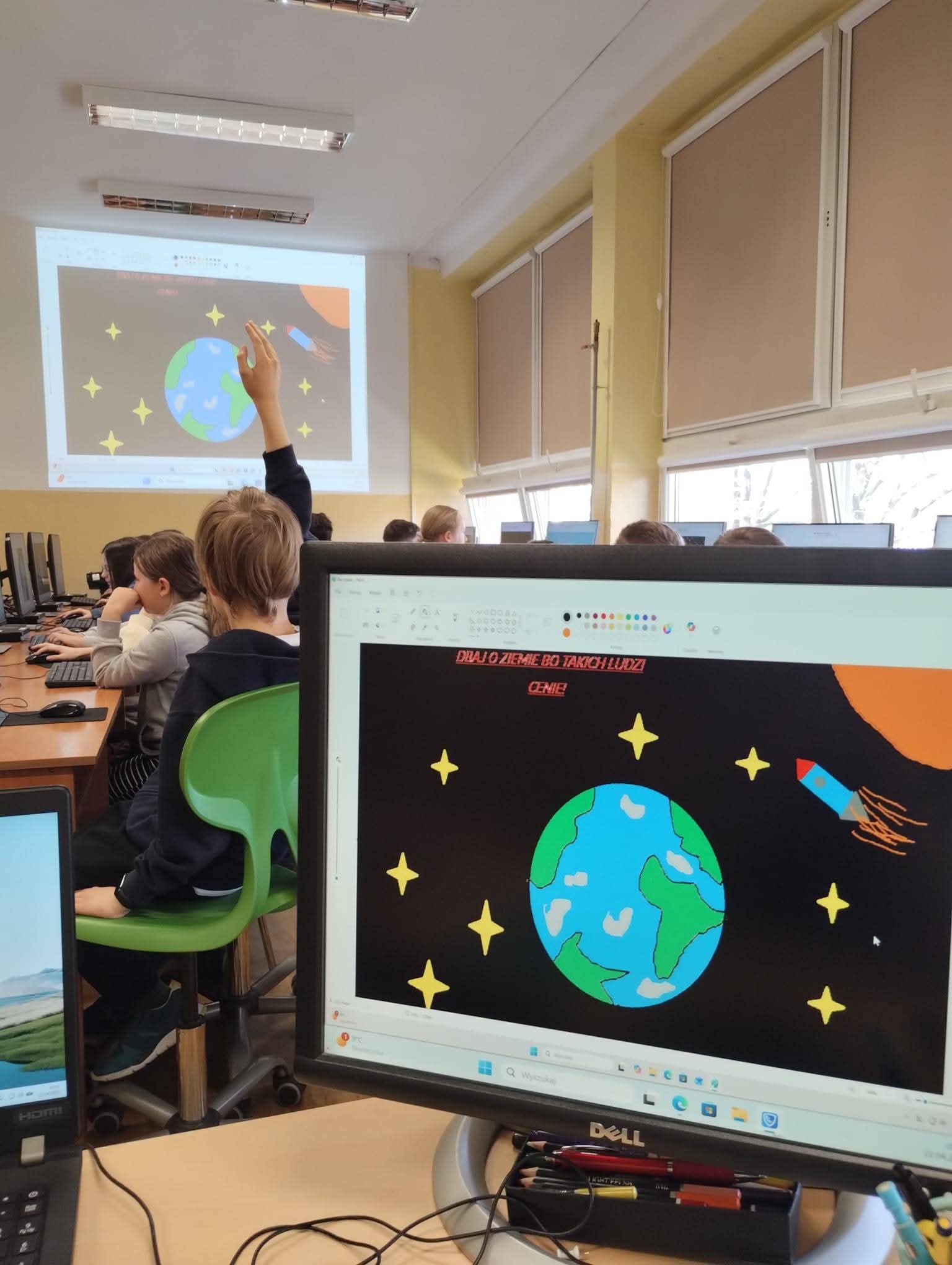 Uczniowie w klasie oglądają prezentację o kosmosie z Ziemią i rakietą.