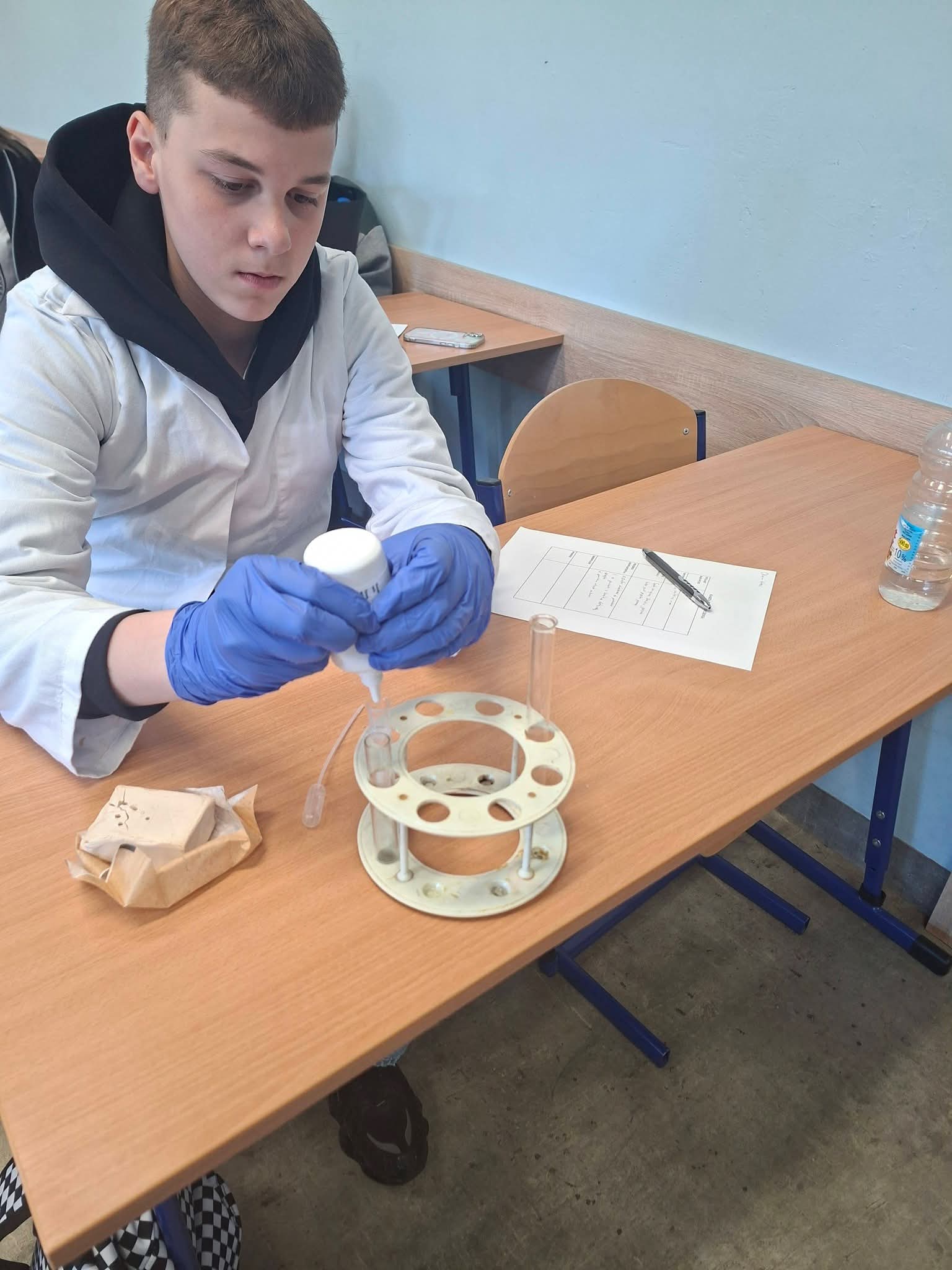 Chłopiec w fartuchu laboratoryjnym wykonuje doświadczenie chemiczne przy biurku.