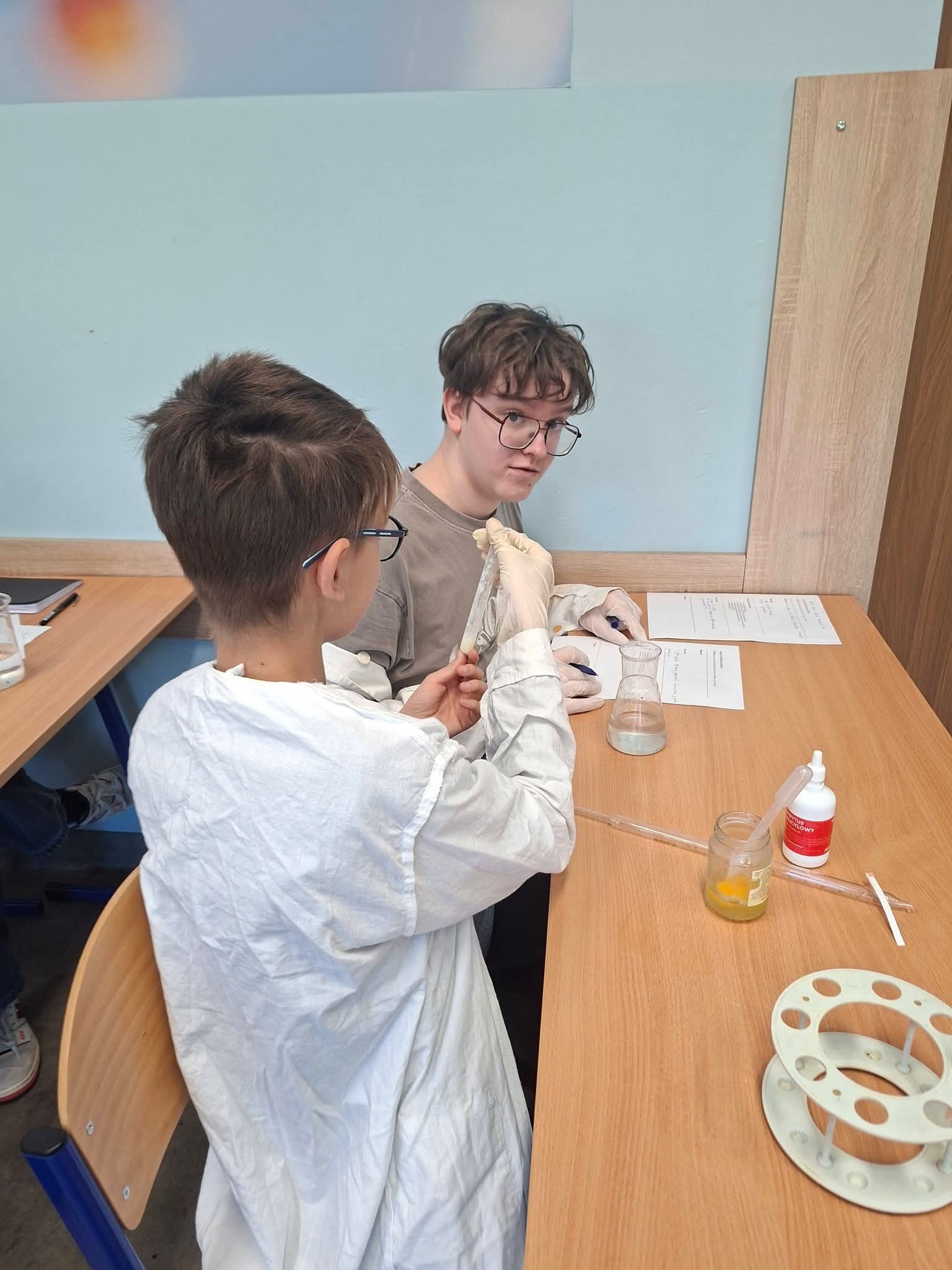 Dwóch chłopców w okularach prowadzi eksperymenty chemiczne w klasie.