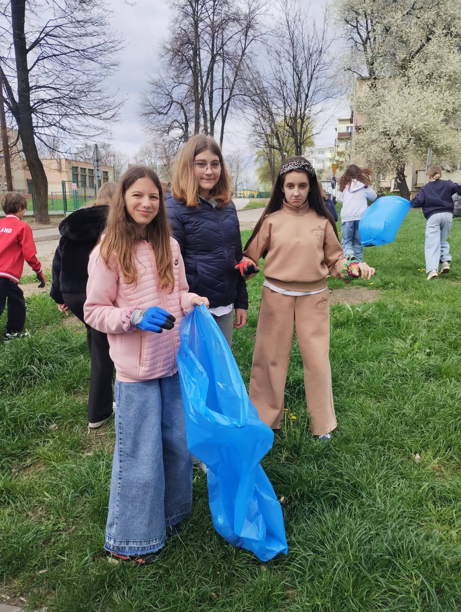 Młode wolontariuszki z niebieskimi workami sprzątają park